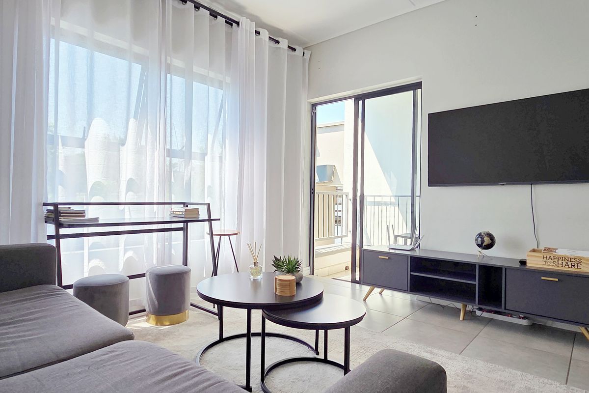 A bright and modern living room featuring large windows, tiled flooring, and a sliding glass door leading to a balcony.