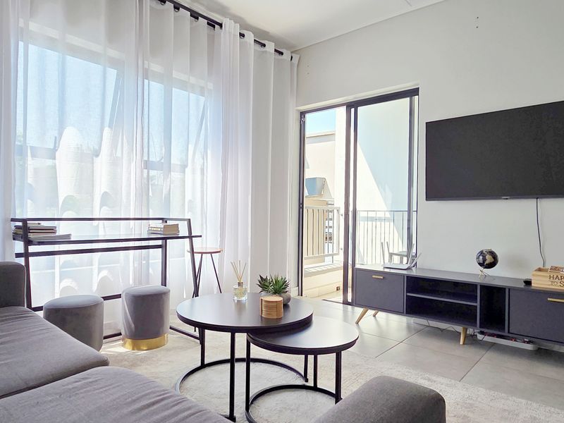 A bright and modern living room featuring large windows, tiled flooring, and a sliding glass door leading to a balcony.