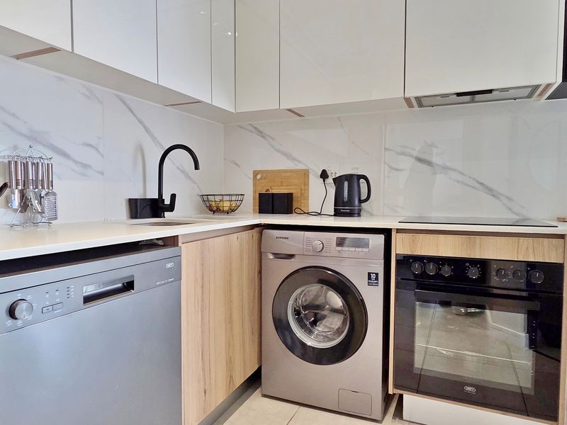 Modern kitchen featuring high-gloss white cabinetry, wood-grain lower cabinets, marble-look splashback, and integrated appliances including an oven, dishwasher, and washing machine.
