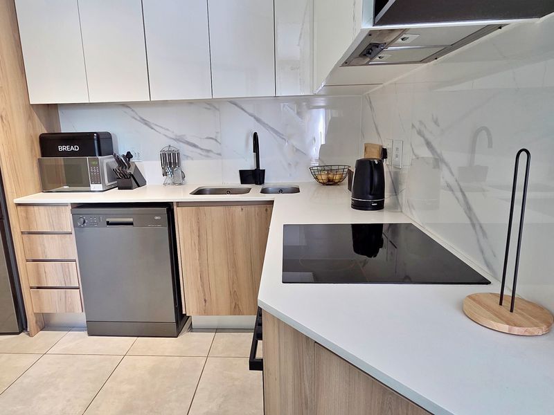 Modern kitchen featuring wood-grain cabinetry, white stone countertops, marble-look splashback, induction hob, and high-quality finishes throughout.