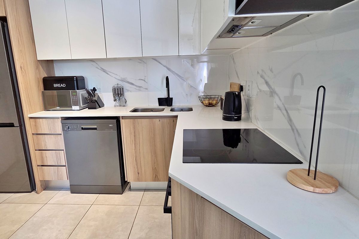 Modern kitchen featuring wood-grain cabinetry, white stone countertops, marble-look splashback, induction hob, and high-quality finishes throughout.