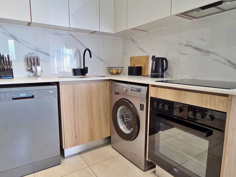 Modern kitchen featuring wood-grain cabinetry, stone countertops, marble-look splashback, and integrated appliances including an oven, hob, and extractor fan.