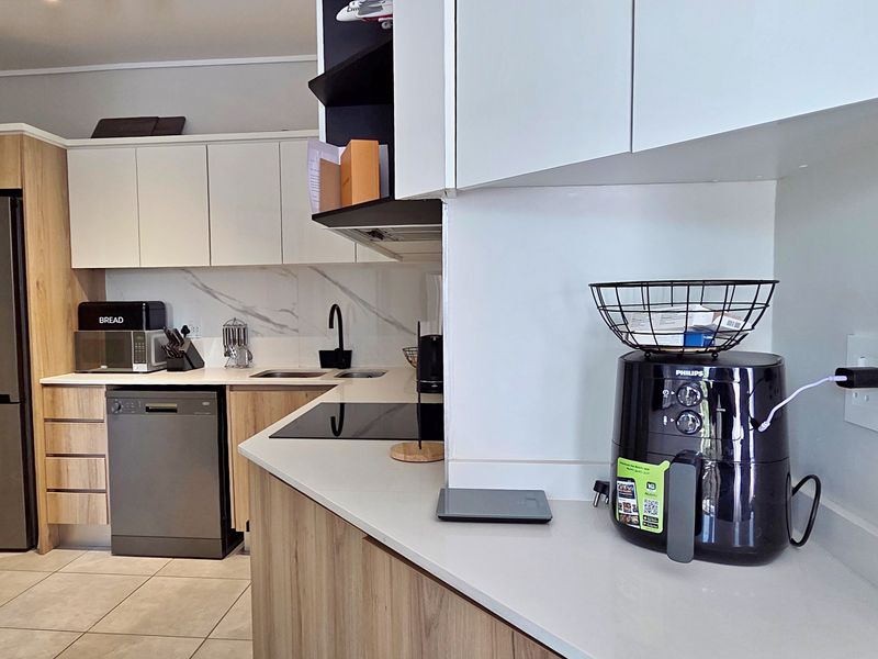 Modern kitchen featuring light wood-tone cabinetry, stone countertops, marble-look splashback, and integrated appliances including a hob and extractor fan.