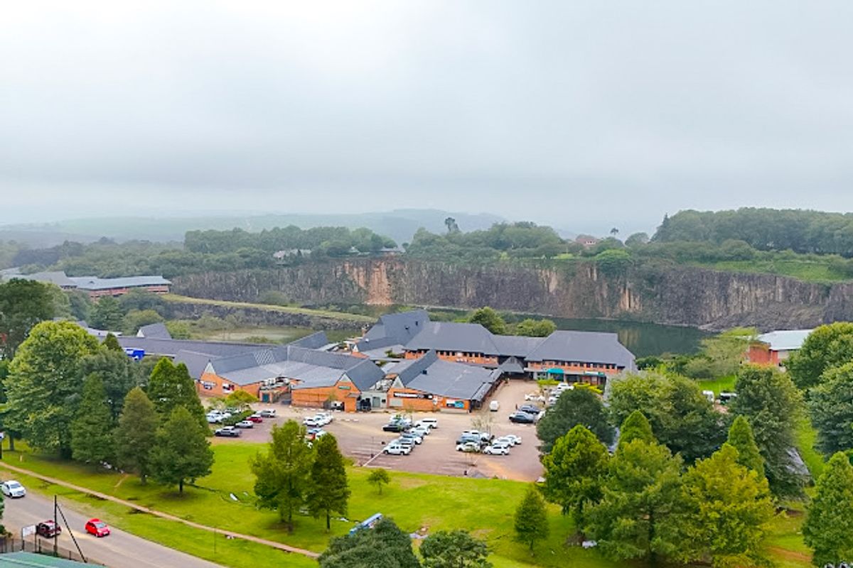An aerial view of a commercial or residential complex featuring multiple buildings with pitched roofs, a paved parking area, and surrounding landscaped grounds.