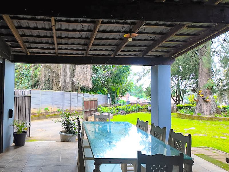 Covered outdoor patio featuring a timber pergola, tiled flooring, and concrete pillars, overlooking a spacious garden area.