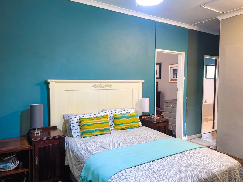 A bedroom featuring laminate flooring, coving, and a ceiling access hatch, with an adjoining en-suite bathroom visible through the doorway.