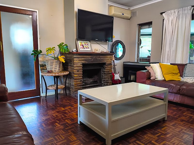 A cozy living room featuring a prominent stone fireplace, classic parquet flooring, and an integrated air conditioning unit.