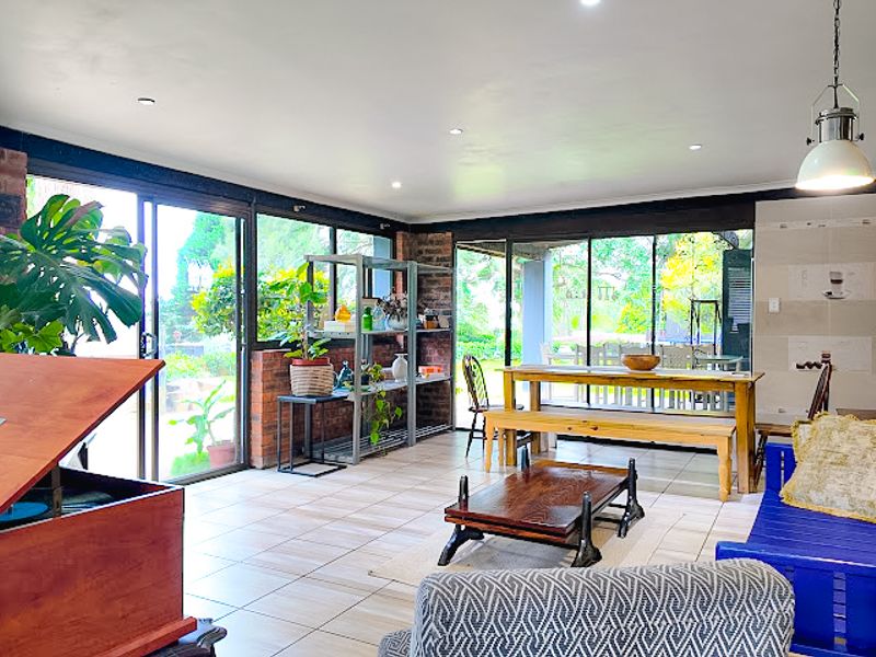 Spacious open-plan living area featuring large sliding glass doors, tiled flooring, exposed brick accents, and recessed lighting, offering a bright and airy atmosphere.