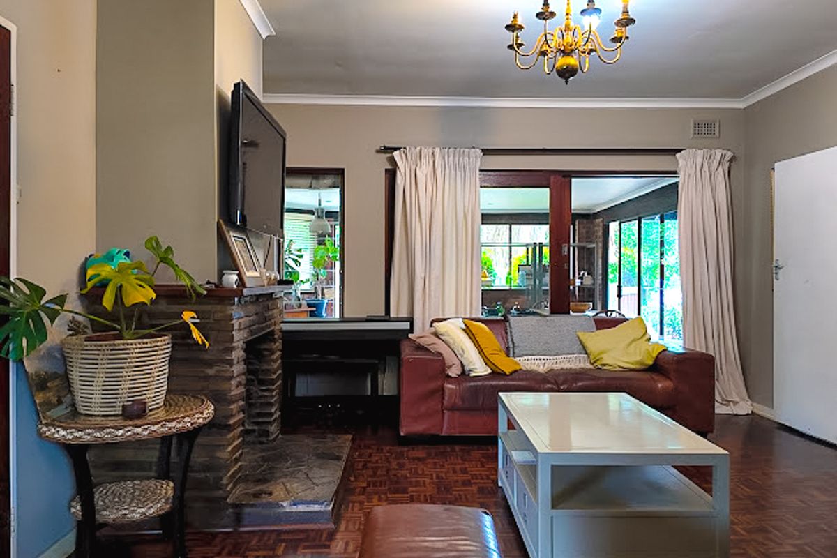A cozy living room featuring a traditional stone fireplace, classic parquet flooring, and large sliding glass doors that provide access to the outdoor area.