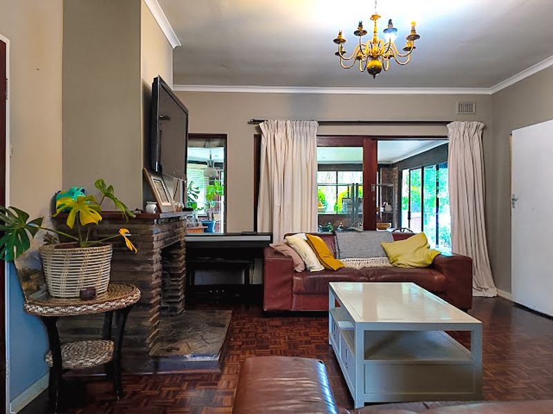A cozy living room featuring a traditional stone fireplace, classic parquet flooring, and large sliding glass doors that provide access to the outdoor area.
