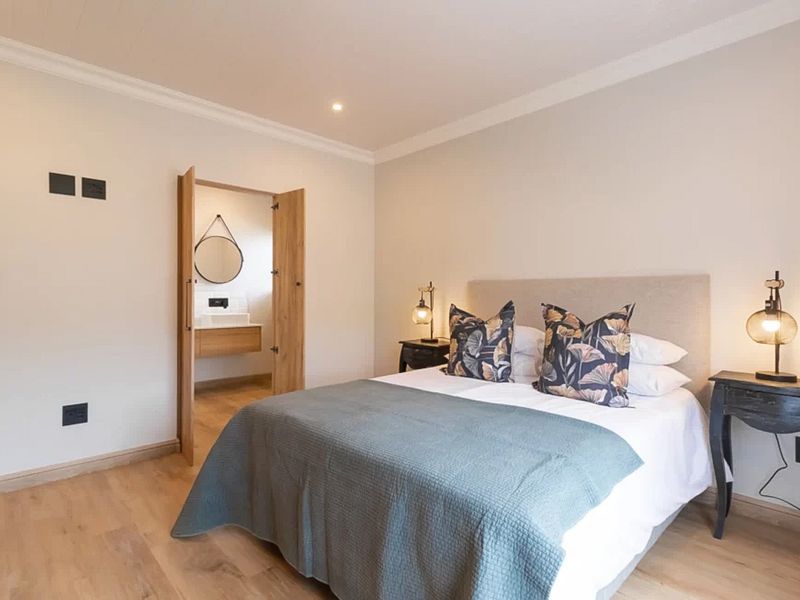 A well-maintained bedroom featuring light laminate flooring, coved ceilings, and direct access to an en-suite bathroom.