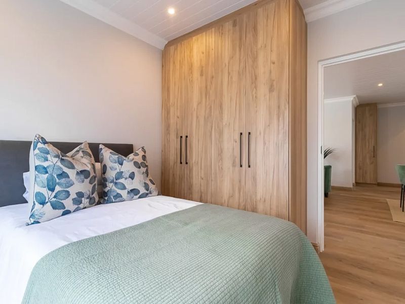 A well-maintained bedroom featuring modern built-in timber cupboards, recessed lighting, and warm timber flooring, with a seamless transition to the adjacent hallway.