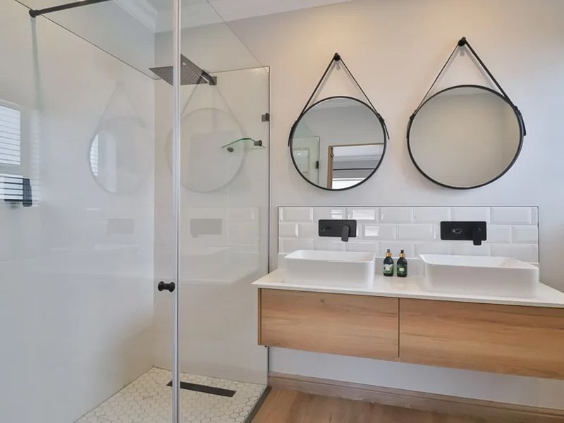 Modern bathroom featuring a floating double vanity with vessel sinks, wall-mounted matte black faucets, subway tile backsplash, and a spacious walk-in shower.