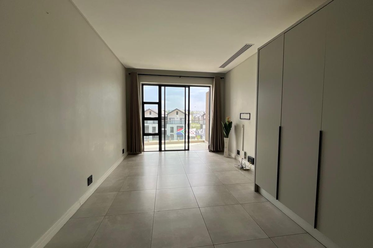 A bright, empty bedroom featuring modern tiled flooring, built-in cupboards, and a sliding glass door leading to a balcony.