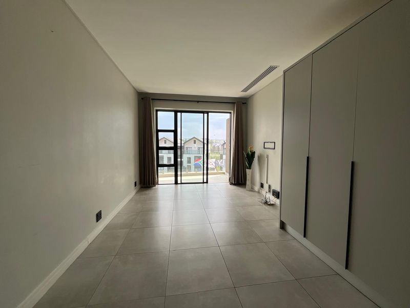 A bright, empty bedroom featuring modern tiled flooring, built-in cupboards, and a sliding glass door leading to a balcony.