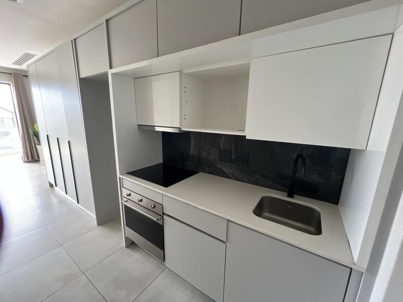 Modern kitchen featuring sleek grey cabinetry, stone countertops, integrated appliances, and a stylish black splashback with a matching mixer tap.
