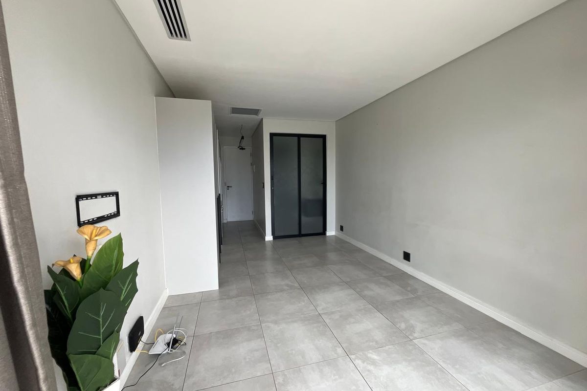 A bright, empty living area featuring modern large-format floor tiles, ducted air conditioning, and a sleek frosted glass door leading to an adjacent space.
