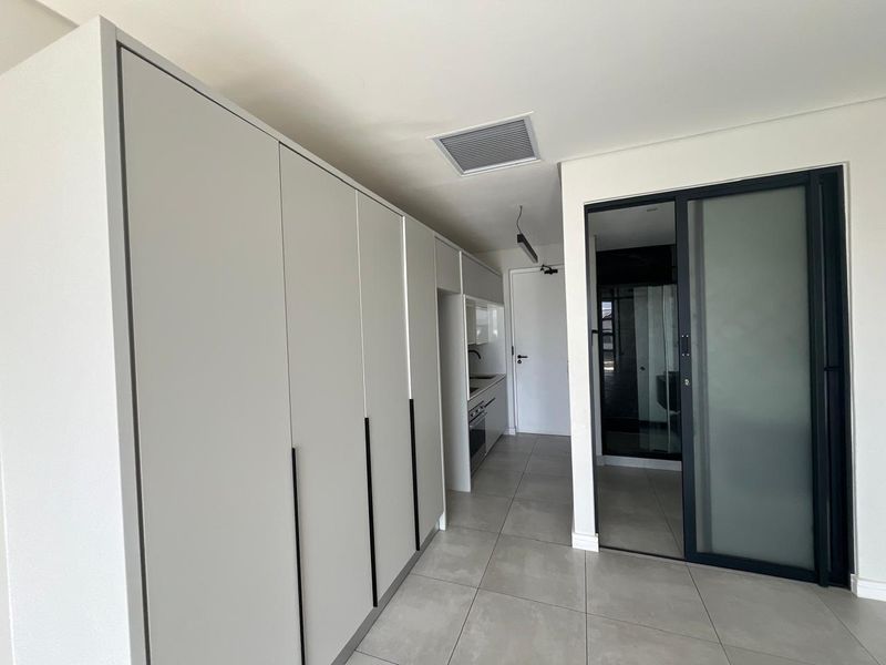 Modern kitchen area featuring sleek built-in cabinetry, integrated appliances, and large format floor tiles, leading to a separate room via a sliding glass door.