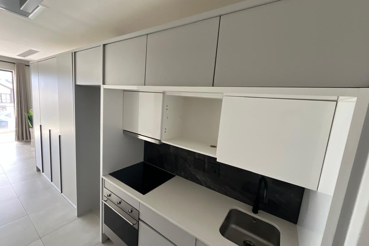 Modern kitchen featuring sleek grey cabinetry, stone countertops, integrated electric hob, oven, and stainless steel sink in a clean, contemporary open-plan layout.