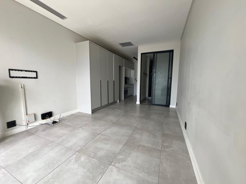 A modern, open-plan living area featuring neutral tiled flooring, built-in cabinetry, and a sleek glass-panelled door, offering a clean and contemporary blank canvas.