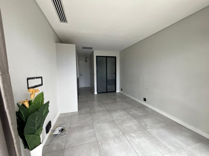 A bright, empty living area featuring modern large-format floor tiles, ducted air conditioning, and a sleek frosted glass door leading to an adjacent space.
