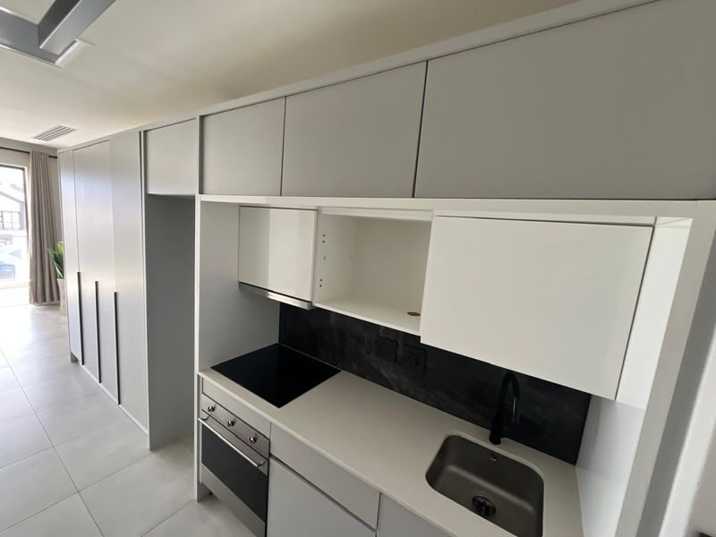 Modern kitchen featuring sleek grey cabinetry, stone countertops, integrated electric hob, oven, and stainless steel sink in a clean, contemporary open-plan layout.