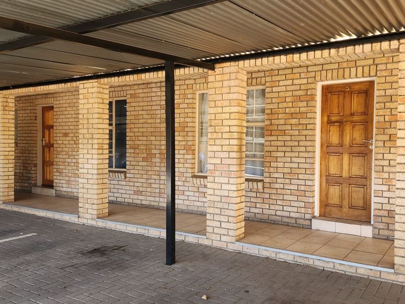 Exterior view of an apartment complex featuring a covered carport, facebrick facade, and individual timber entrance doors.