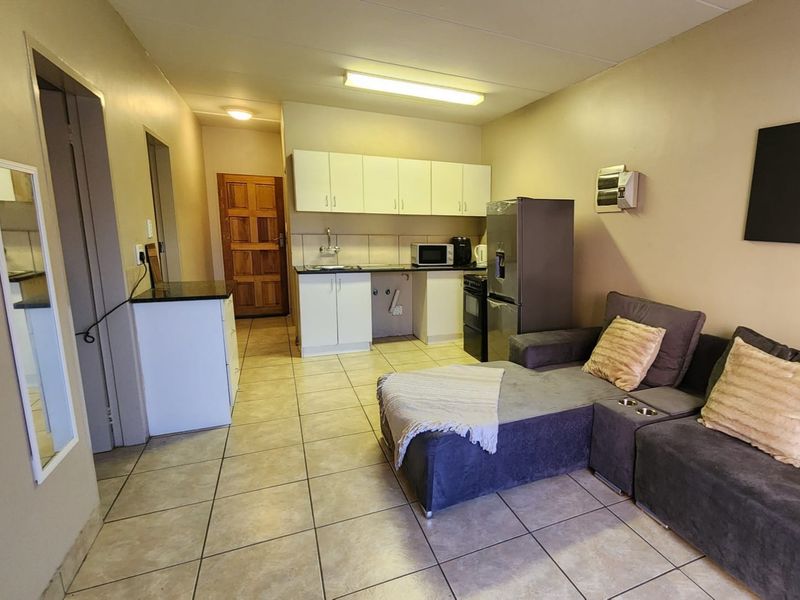 Open-plan living area featuring a compact kitchen with built-in cabinetry, tiled flooring, and direct access to the entrance.