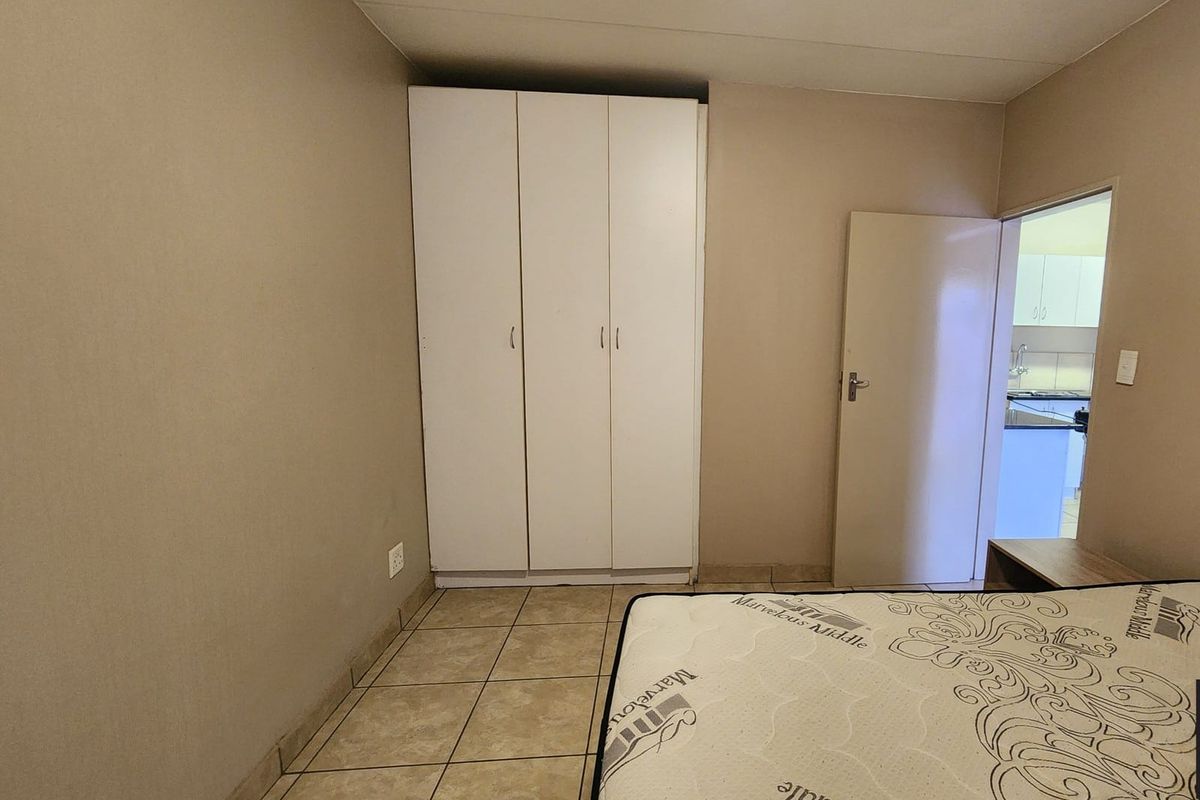 A bedroom featuring tiled flooring and a built-in white wardrobe, with an adjacent doorway leading to a kitchen area.