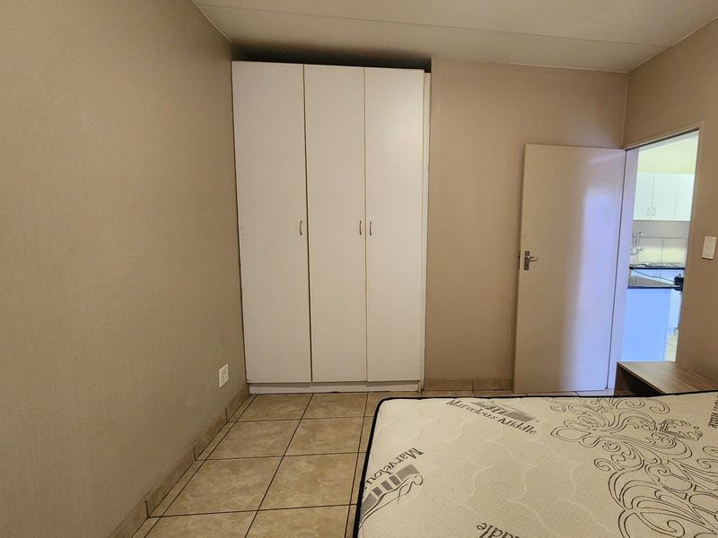 A bedroom featuring tiled flooring and a built-in white wardrobe, with an adjacent doorway leading to a kitchen area.