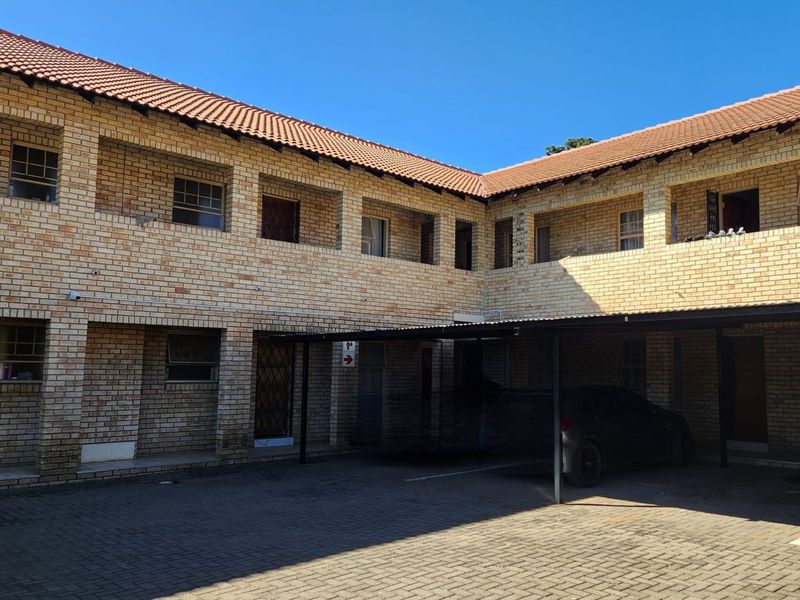 Exterior view of a face brick apartment complex featuring covered parking bays and a paved driveway area.