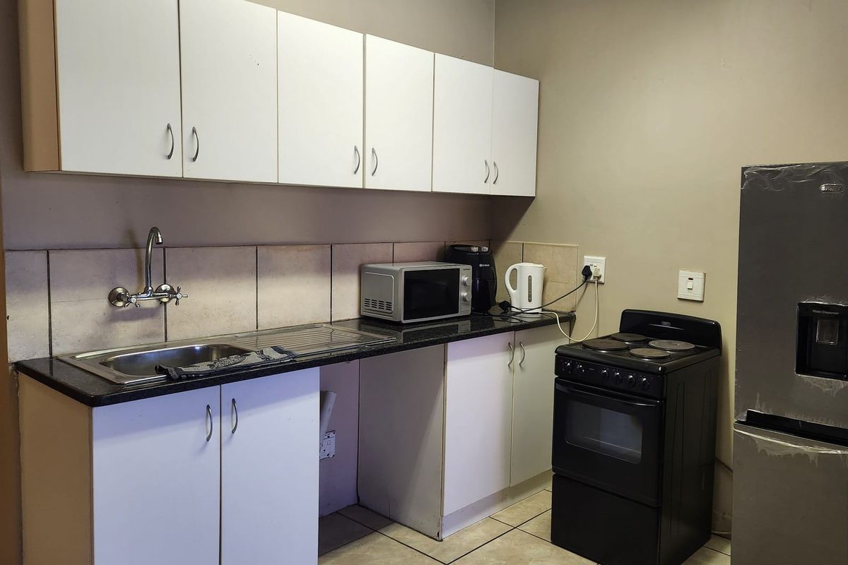 Compact kitchen featuring white cabinetry, granite countertops, tiled backsplash, and a freestanding electric stove.
