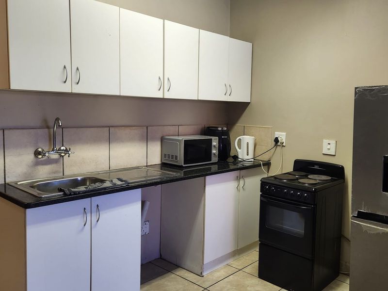 Compact kitchen featuring white cabinetry, granite countertops, tiled backsplash, and a freestanding electric stove.