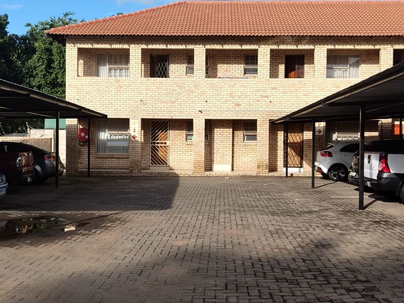 Front view of a two-story face brick apartment complex featuring covered parking bays and a paved driveway.