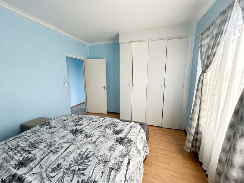 A bedroom featuring light blue walls, laminate flooring, and a white built-in wardrobe with ample storage space.