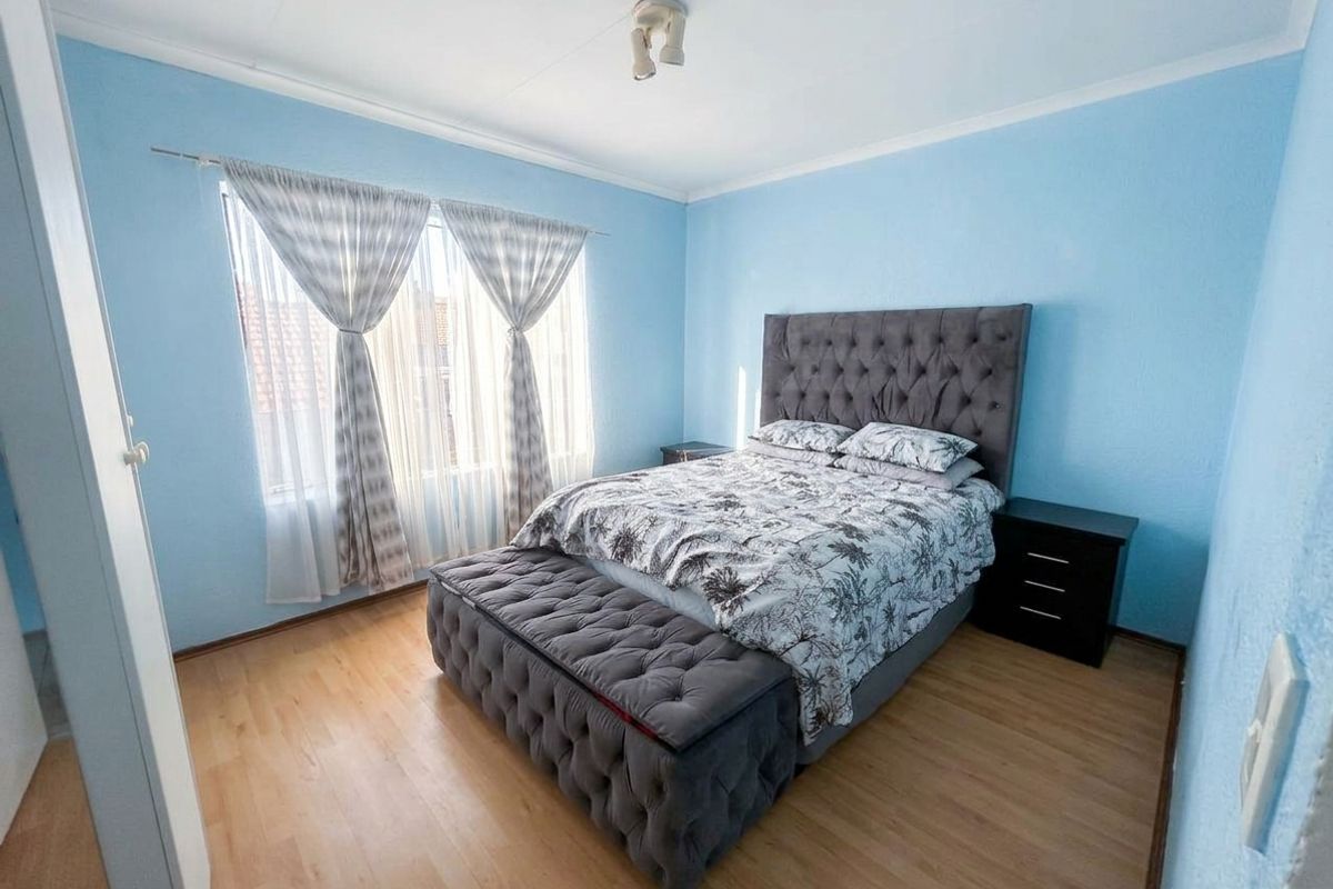 A well-lit bedroom featuring light-toned laminate flooring, blue painted walls, and a built-in cupboard, offering a comfortable and functional living space.