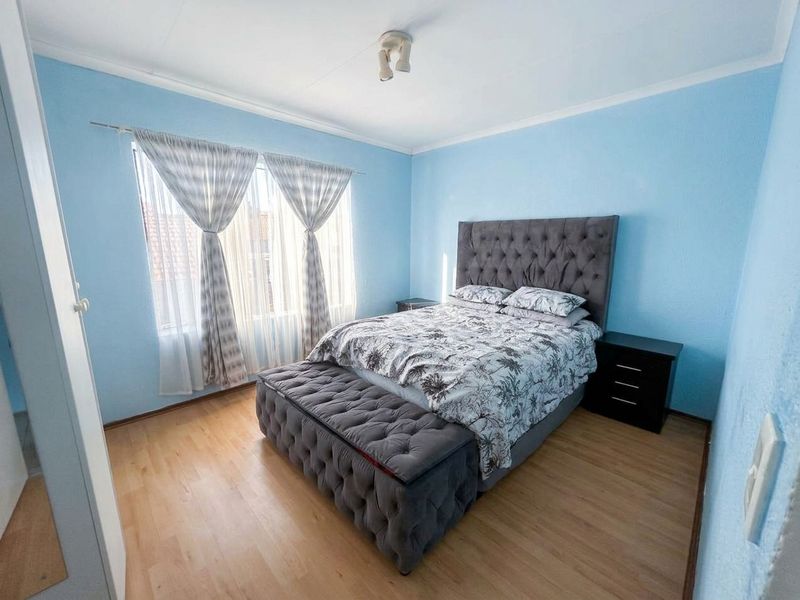 A well-lit bedroom featuring light-toned laminate flooring, blue painted walls, and a built-in cupboard, offering a comfortable and functional living space.