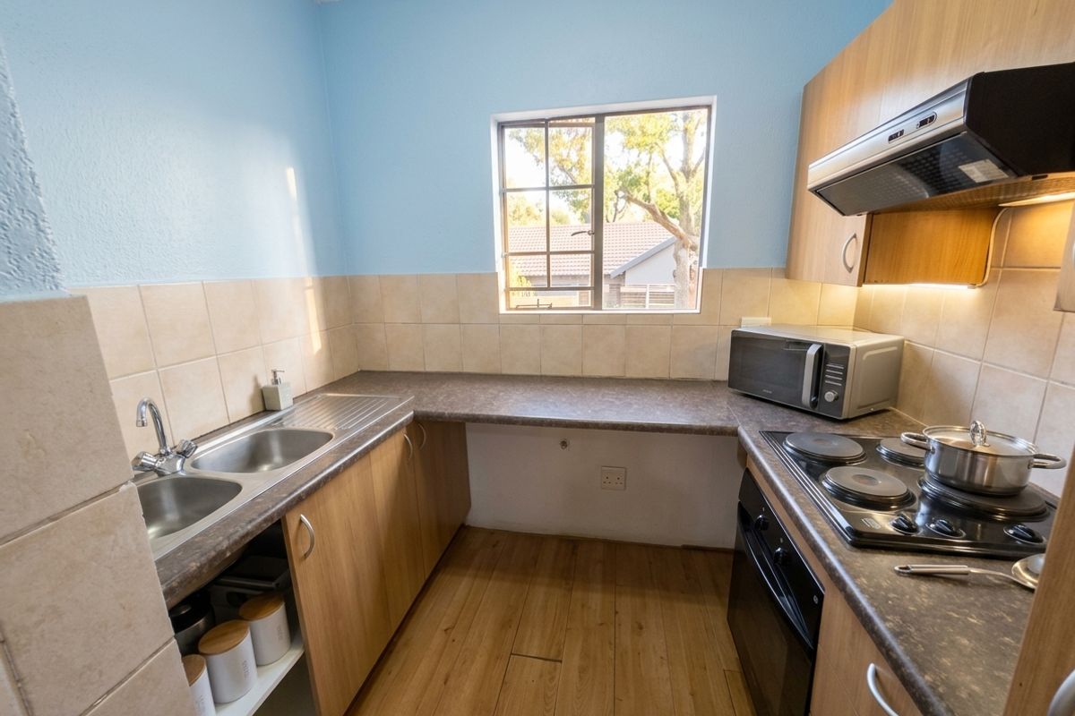 A functional kitchen featuring laminate countertops, built-in cabinetry, a double bowl sink, and integrated cooking appliances with a tiled splashback.