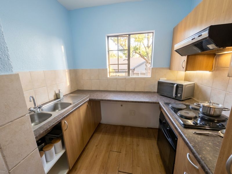 A functional kitchen featuring laminate countertops, built-in cabinetry, a double bowl sink, and integrated cooking appliances with a tiled splashback.