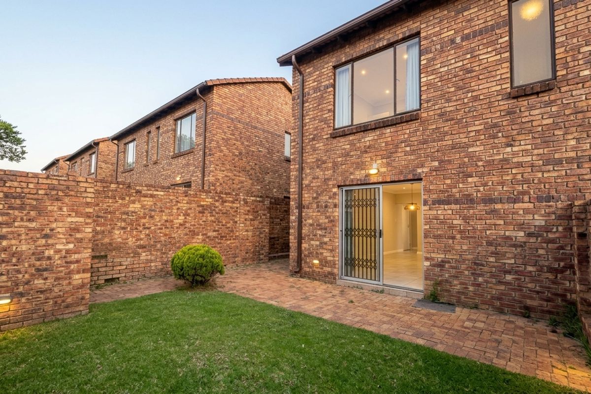 Rear view of the townhouse featuring a face brick facade, paved patio area, and a sliding glass door with security gate access.