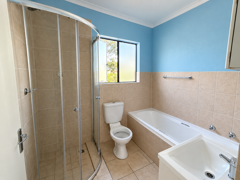 A clean, functional bathroom featuring a separate shower enclosure, bathtub, toilet, and vanity basin with neutral wall and floor tiling.
