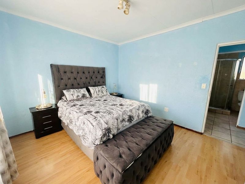 A bedroom featuring laminate flooring and an en-suite bathroom, with light blue walls and a coved ceiling.