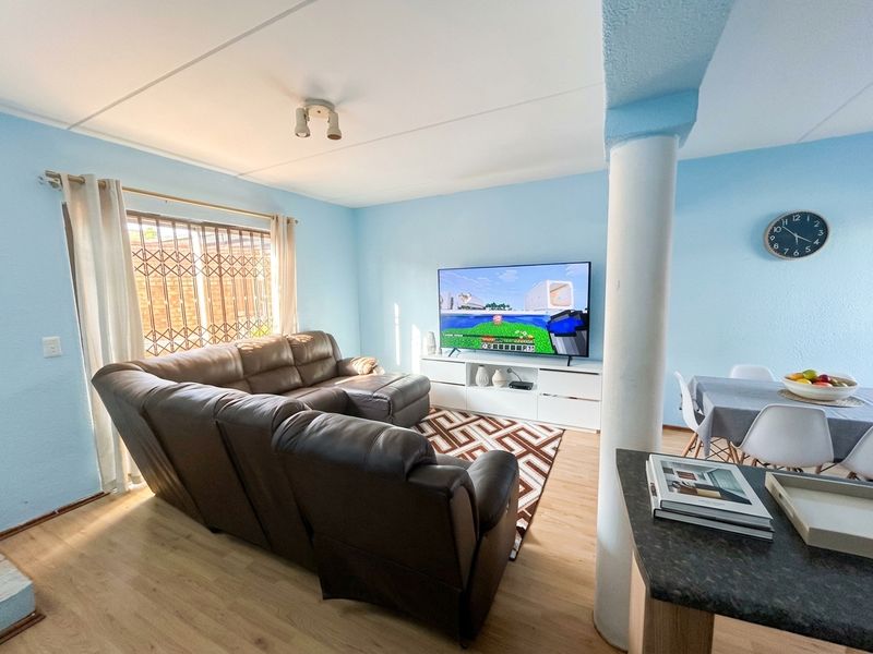 Open plan living and dining area featuring laminate flooring, a structural column, and natural light through a window with a security gate.