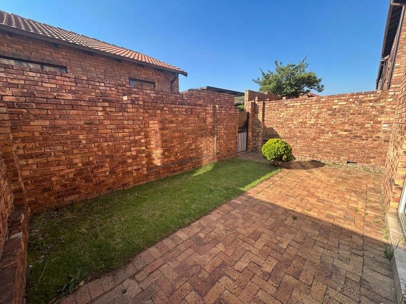 A private rear courtyard featuring a brick-paved patio area, a small lawn, and high brick boundary walls for added privacy.
