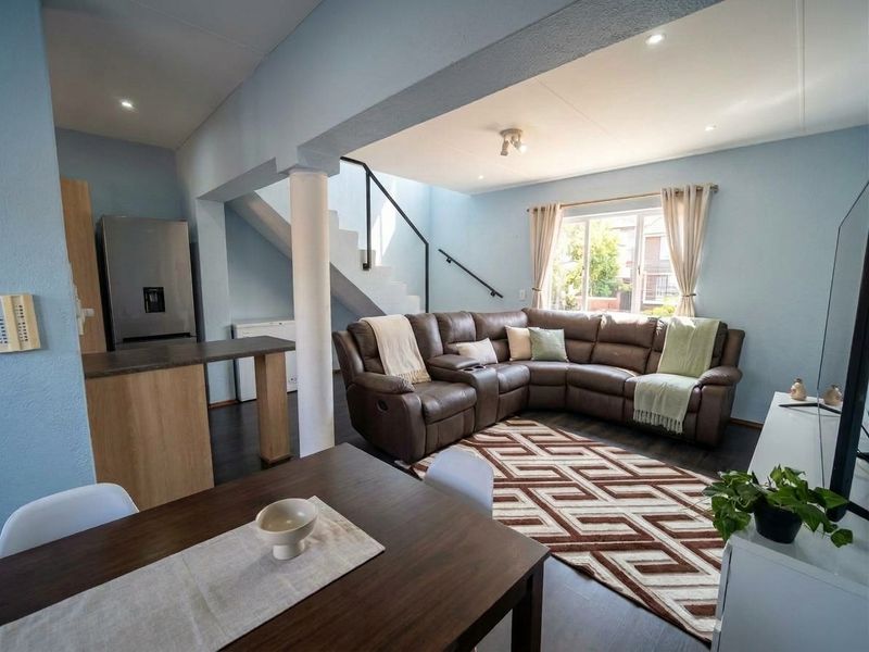 Spacious open-plan living and dining area featuring modern laminate flooring, recessed lighting, and a staircase with a contemporary metal handrail.