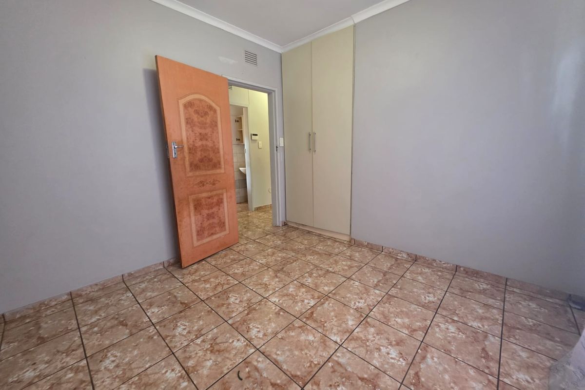 An empty bedroom featuring tiled flooring, a built-in wardrobe, and neutral wall finishes, with an adjacent view into a bathroom area.