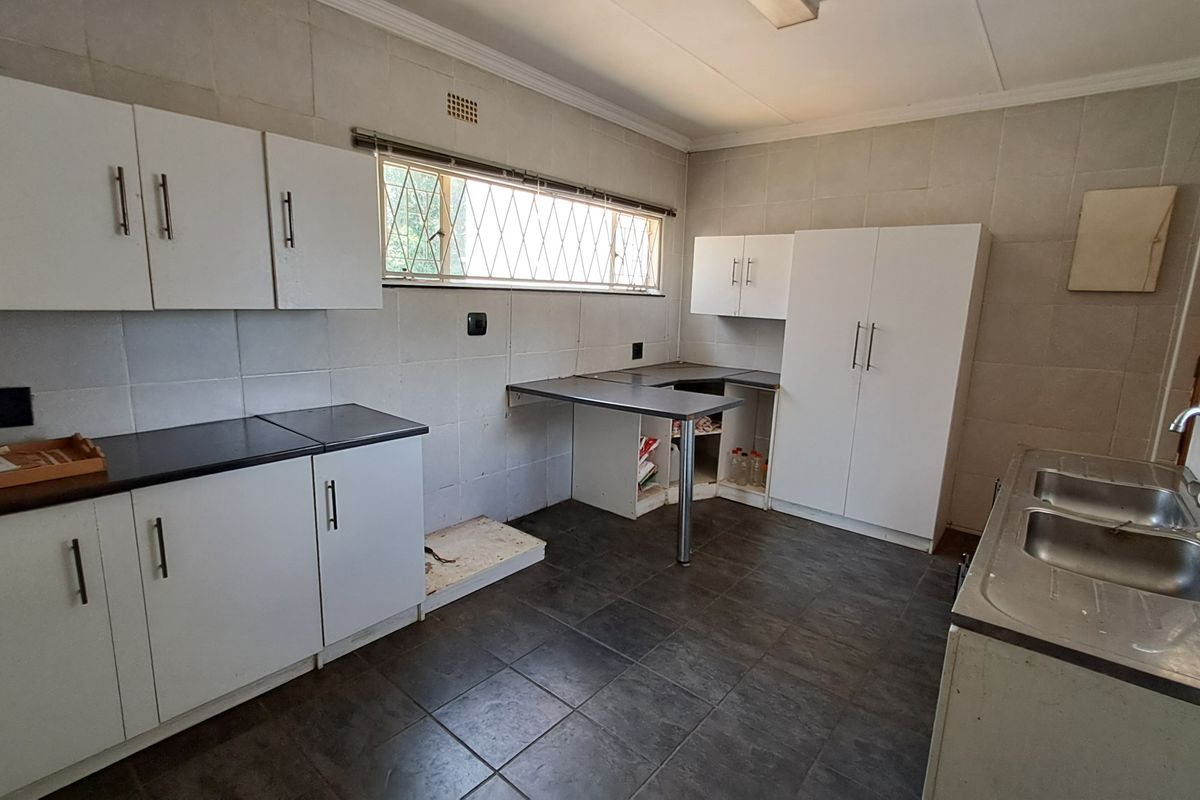 A functional kitchen featuring white cabinetry, dark laminate countertops, tiled walls, and a double bowl stainless steel sink with security bars on the windows.