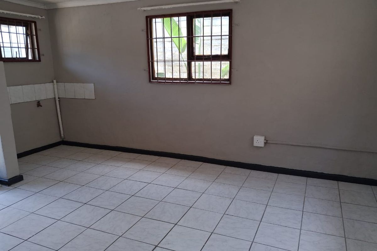 An empty, functional room featuring tiled flooring, security bars on windows, and basic wall-mounted electrical and plumbing provisions.