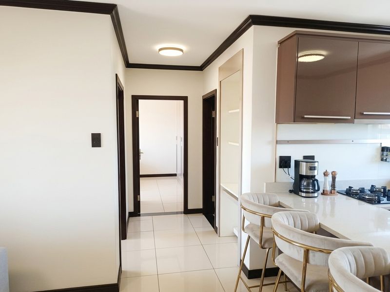 Modern open-plan kitchen area featuring sleek cabinetry, stone countertops, and a gas hob, seamlessly transitioning into a hallway with tiled flooring.