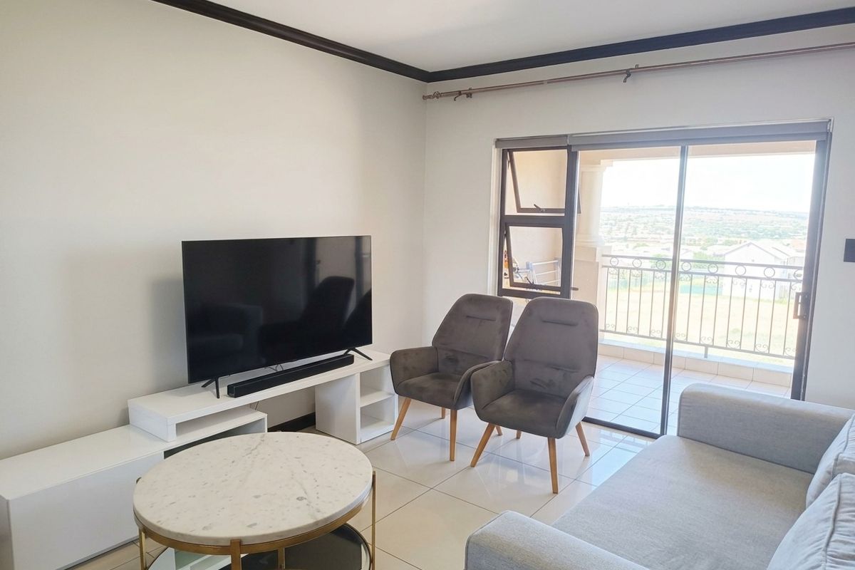 A bright living room featuring tiled flooring, crown molding, and a sliding glass door providing direct access to a balcony with scenic views.